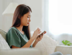 ソファーに座りスマートフォンを操作する女性の写真